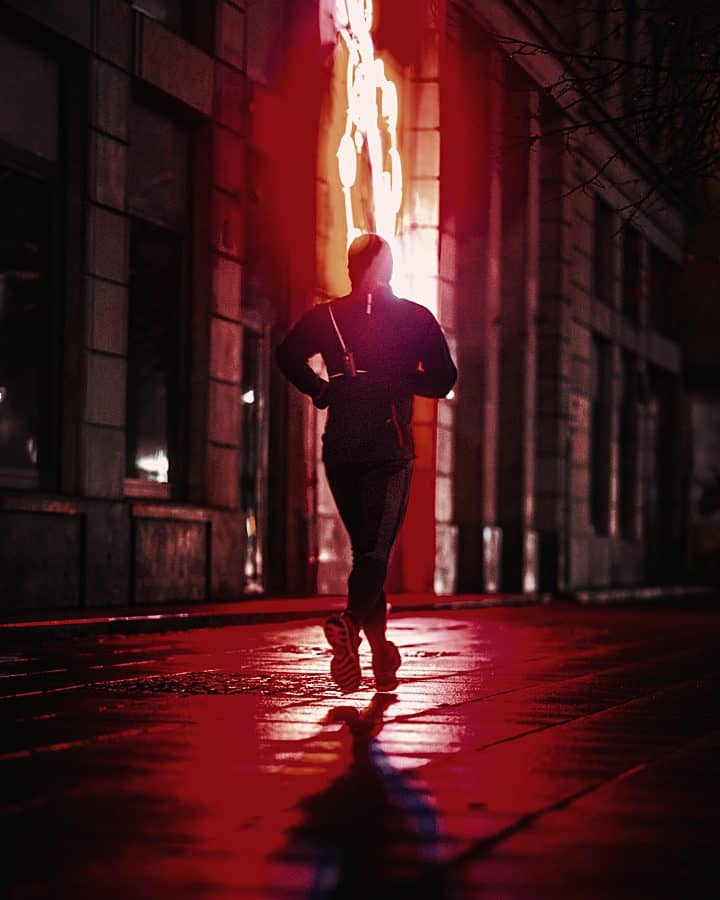 Runner on a wet city street lit by red light at night