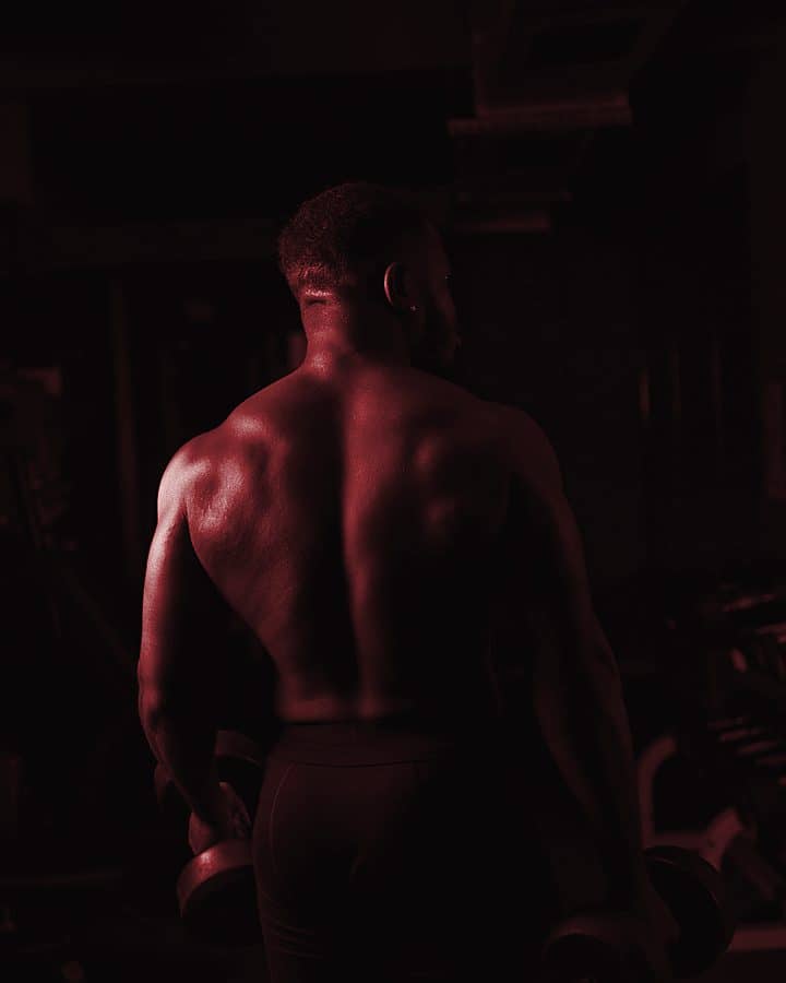 Athlete seen from behind, holding dumbbells in a dark gym