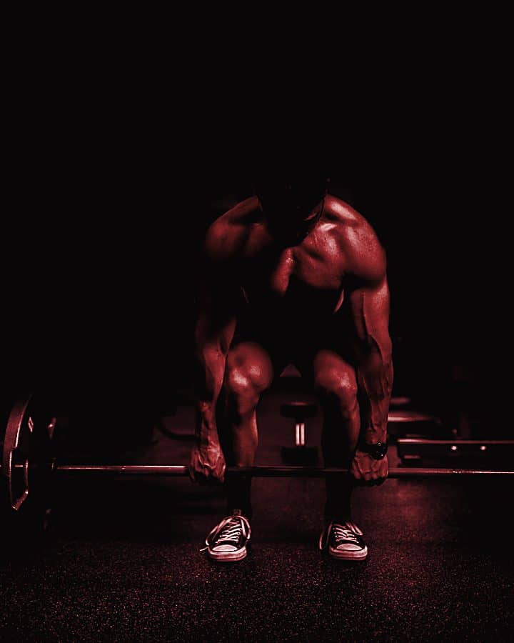 Lifter standing over a loaded barbell in a dark gym